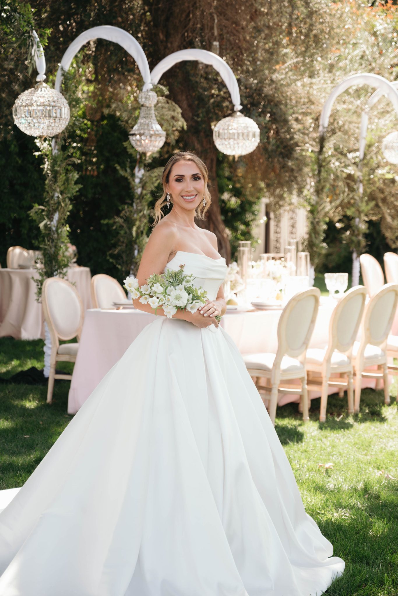 A bride in her styled garden wedding venue holding a bunch of white flowers